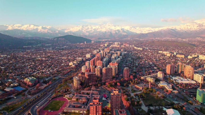 Aerial dolly in of Las Condes neighborhood buildings, snow capped mountains in background at sunset, Santiago, Chile Royalty-Free Stock Footage #1093758063
