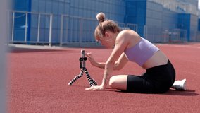 Sports blondie woman training in stadium at summer sunny day use smartphone for recording exercises or online lessons.