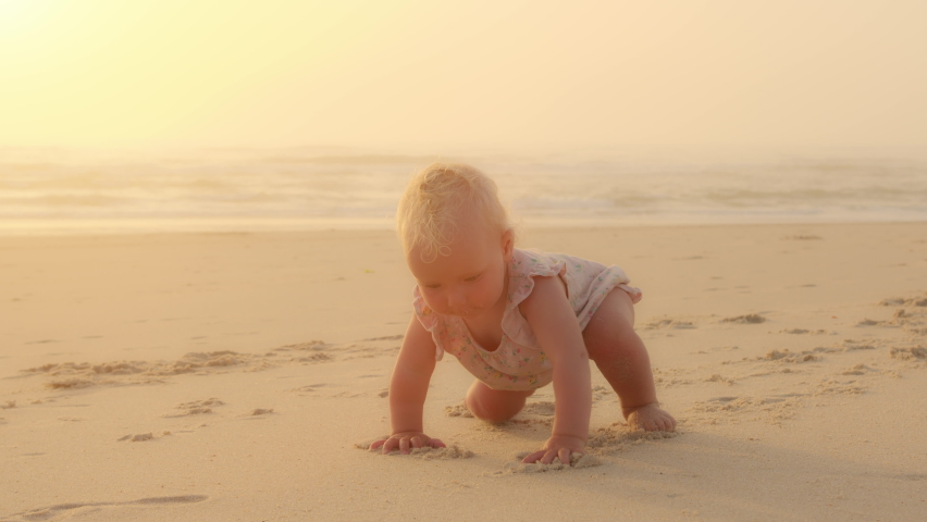 Happy Caucasian little baby crawl alone on knees outdoors on sand seaside coast. Infant small girl boy daughter toddler child kid learns crawling quickly learning walks on beach near ocean on Royalty-Free Stock Footage #1093772621