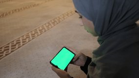 Hijab muslim woman green screen smarthphone, watch phone screen on mosque, islamic image with the theme of watching an videos with a phone indoors