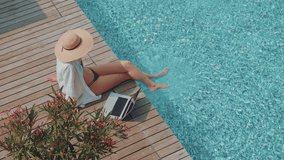 A young entrepreneur woman is working on her computer in by the resort pool in summer time. Remote working anywhere, the concept of digital nomad. Top travel destination. - Powered by Shutterstock - Get 15% off with code: PIKWIZARD15