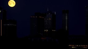 A full orange moon orbits and hides behind skyscrapers in the nighttime center of Warsaw - Powered by Shutterstock - Get 15% off with code: PIKWIZARD15