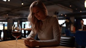 Pretty smiling young woman sitting at restaurant with red wine and using typing message on smartphone while having evening alone. Happy lady browsing, reading news, chatting with boyfriend. - Powered by Shutterstock - Get 15% off with code: PIKWIZARD15