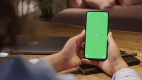 Chroma Key Without Touching or Swiping. Back View of Woman Holding Green Screen Smartphone Watching Content. Girl Using Mobile Phone sitting in the living room in the evening, Browsing Internet