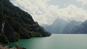A picturesque lake in Switzerland between mountains overgrown with greenery, the tops of which are covered with white clouds. Lakeside town in the Alps, drone video