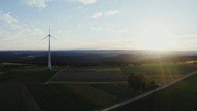 The wind farm stands among the striped multi-colored fields in the rays of the rising sun. Drone video, view of the picturesque green valley.
