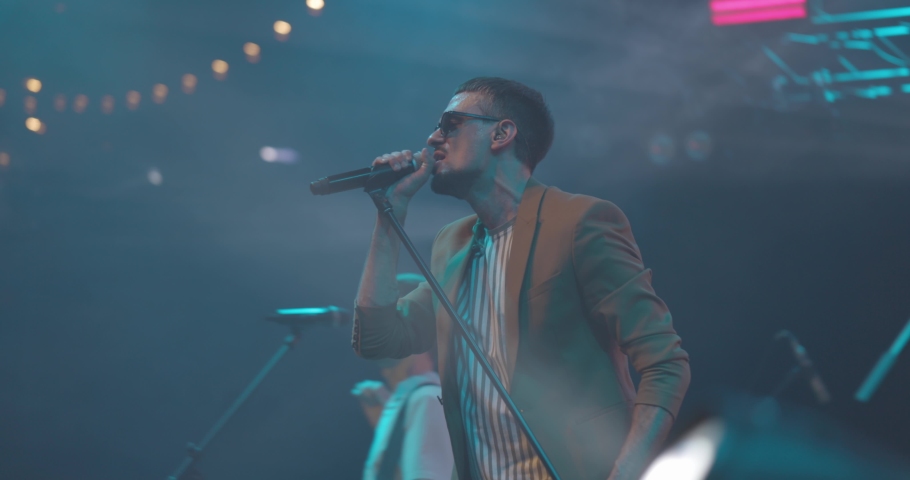 Side view portrait of a man singing to microphone on light background. Stylish cool guy performing concert on stage. Music and concert concept.