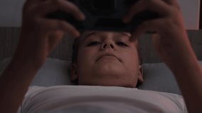 A teenage boy plays mobile games while lying in bed before going to bed.