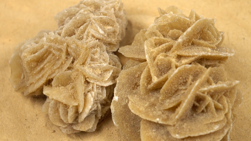 Sample of a desert rose rock mineral stone rotates on a sand background 