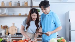 Asian couple using tablet to watch healthy meals online in the kitchen together. Search for recipes on the Internet.