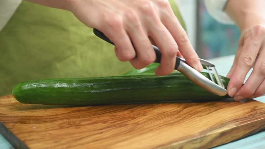 The cook peels the skin of the cucumber.