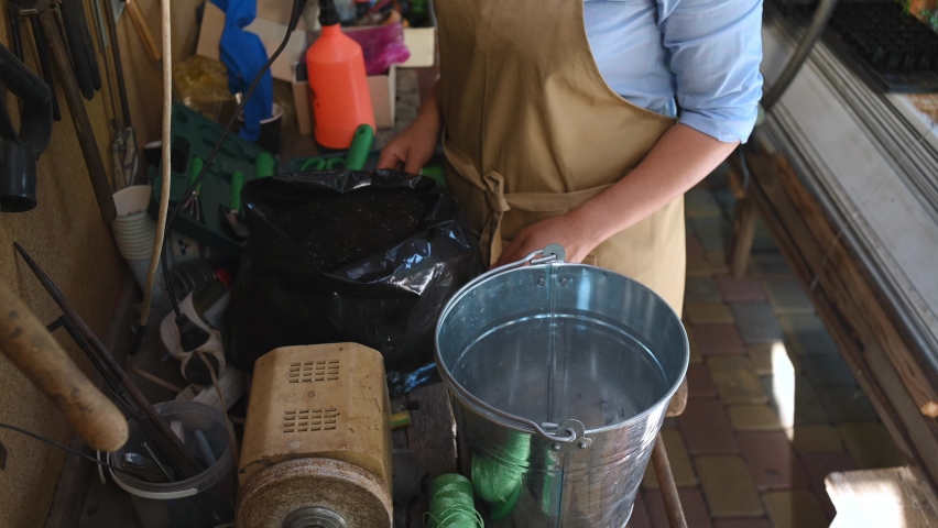Top view. Hands of florist, gardener in beige apron standing at a wooden table with lots of garden tools, sorting fertilized soil with her hands in the summer cottage workshop. Gardening