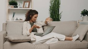A woman freelancer relaxes and communicates with people via video communication while lying on the couch at home with her laptop. Lifestyle in comfort 