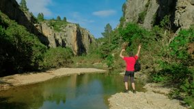Man is dancing with a backpack. Male is hiking in nature. Green forest landscape. Green rocky landscape. Mountain and pond. Beautiful ravine. Horizontal video.