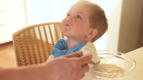 mother feeds porridge to her son. happy family healthy food concept. the boy little son eats porridge with a spoon soiled in his face. child dirty dirty funny eating porridge himself video lifestyle