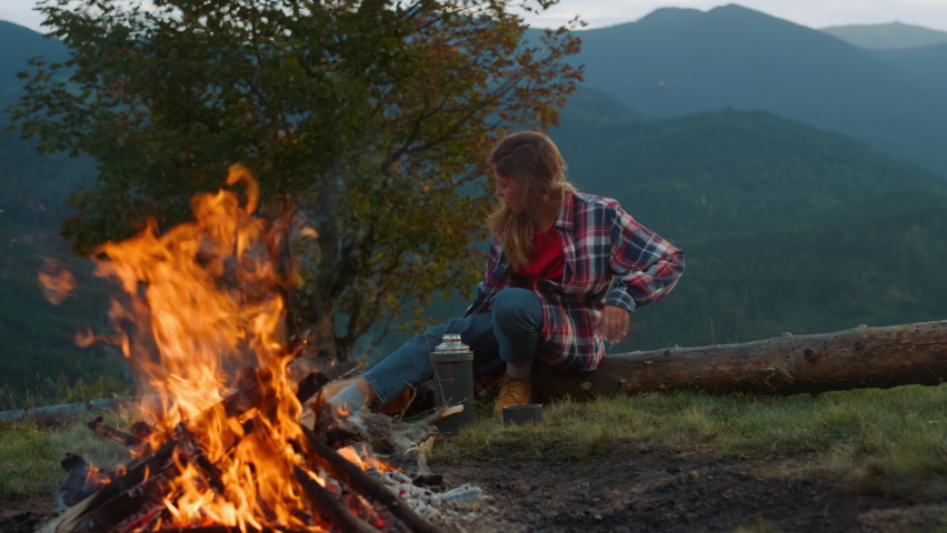 Active woman spend evening by bonfire. Young hiker play acoustic guitar in mountains green hill close up. Positive millennial rest on nature landscape. Traveler musician perform outside. Relax
