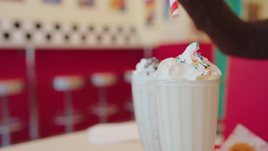 Closeup of hand putting paper drinking straw in milkshakes with whipped cream in glass, Delicious dessert drink. Royalty-Free Stock Footage #1093817483