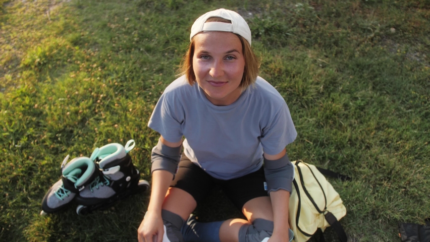 Attractive young woman sitting on lawn look at camera smiling in summertime. Healthy lifestyle and sports concept. Skating roller portrait.