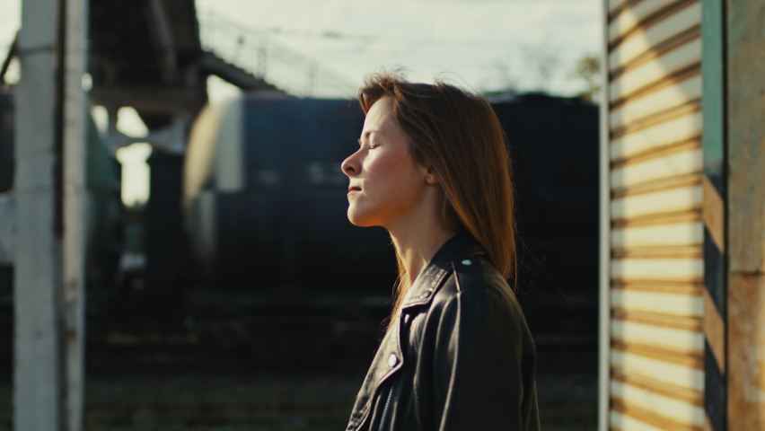 Beautiful woman stands thoughtfully with her eyes closed at the train station