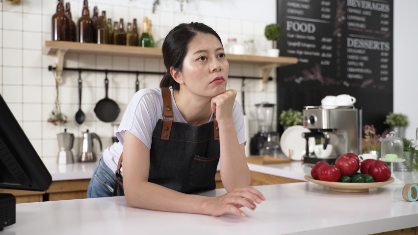 portrait of a bored asian waitress tapping finger and propping head on the counter while waiting for clients to visit the restaurant during pandemic outbreak Royalty-Free Stock Footage #1093828571