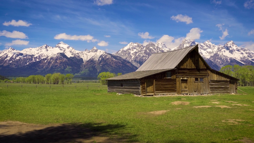 Pan right of Historic John Moulton Barn at Mormon Row in Grand Teton National Park on a sunny summer day, with snowcapped Teton Mountain Range in the background. 4K UHD video.