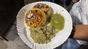 Video depicts a man holding a plate of savory litti chokha smeared with ghee and served with roasted mashed eggplant or baingan bharta and a green spicy chutney.