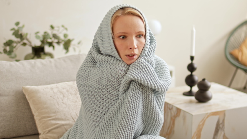 A young woman is freezing and shivering from the cold, hiding herself in a warm blanket knitted plaid have to problems with central heating and heat outage at home in winter. Royalty-Free Stock Footage #1093843855