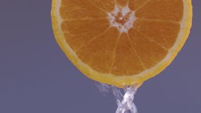 Water drips flowing from a sliced sweet and fresh orange down on a grey background, fruit for frash and natural juice, cold diet drink with vitamin c. Slow motion, filmed on cinema camera, 4K.