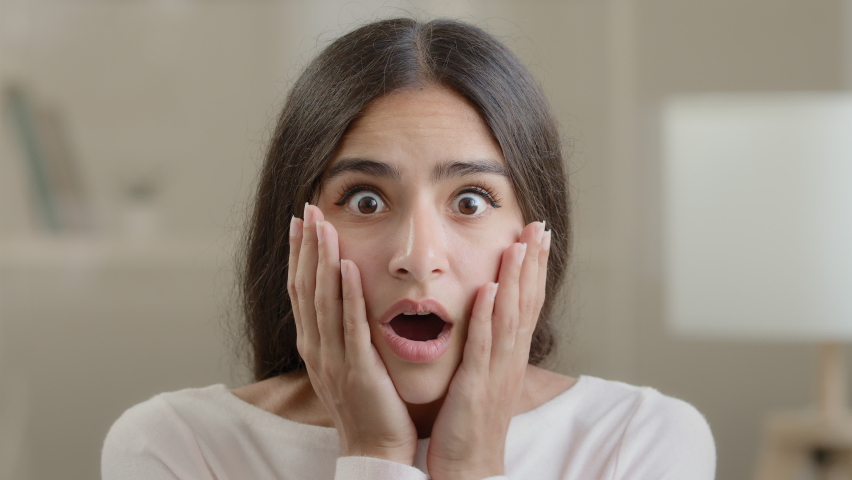 Afraid emotional girl brunette woman negative shocked frightened arabian young lady hold head with hands open mouth feel horror terrified facial emotion looking at camera panic confusion bad