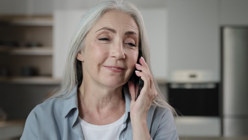 Old happy smiling woman housewife 60s grey-haired senior lady granny talk mobile phone with grandchildren family answer call booking online remotely conversation use telephony communication share