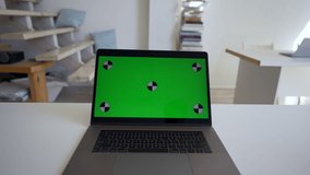 Modern laptop with green chromakey screen stands on office table against stairs. Open electronic device at workplace ready for tracking closeup