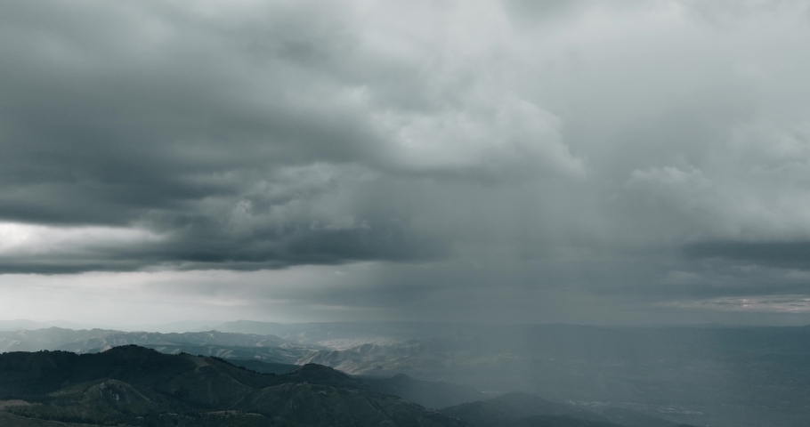 Aerial of storm clouds raining down on mountain range.