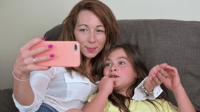 Happy mother with her daughter are making a video call to father or relatives in a sofa. Concept of technology, new generation, family, connection, parenthood. High quality 4k footage
