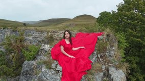 A girl in a red dress sits on the edge of a cliff, summer, mountains and forest, a seed from a drone