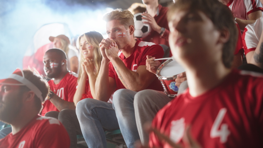 Sport Stadium Event: Handsome Caucasian Man Cheering. Crowd of Fans with Painted Faces Shout for their Red Soccer Team to Win. Scoring a Goal Celebration, Championship Victory. Low Angle Tribune Shot