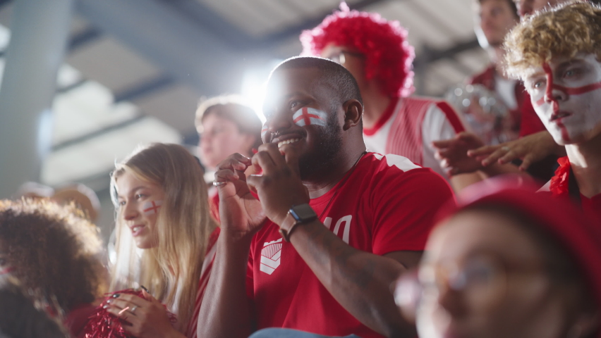 Sport Stadium Big Event: Handsome Expressive Black Man with Painted face Jumping Up and Cheering Goal Score. Crowd of Fans Shout for Red Soccer Team to Win. People Celebrate Championship Victory | Shutterstock HD Video #1093867137