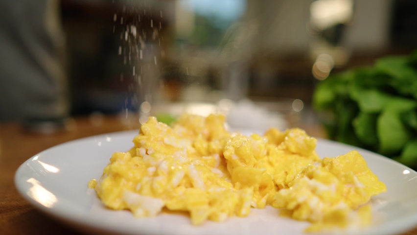 Sprinkling salt on a plate of delicious bight yellow scrambled eggs in the kitchen Royalty-Free Stock Footage #1093870203