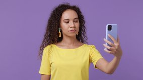 Young woman of African American ethnicity 20s she wear yellow t-shirt doing selfie shot on mobile phone post photo on social network isolated on plain pastel light purple background studio portrait