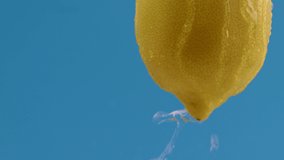 Water drips flowing from a whole sour and fresh lemon down on a blue background, fruit for frash and natural juice, cold diet drink with vitamin c. Slow motion, filmed on cinema camera, 4K.