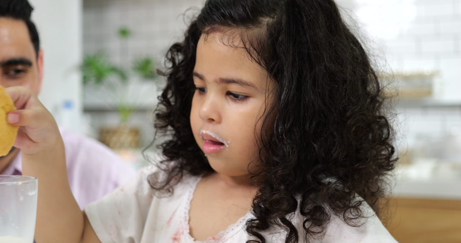 Playful little girl tasting cookie with milk in kitchen, Little daughter and father cooking in kitchen, Happy family in kitchen, Junior chef with homemade food and dessert