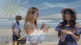 Composite video of waving argentina flag over two caucasian women enjoying drinks at the beach. Global tourism and travel concept
