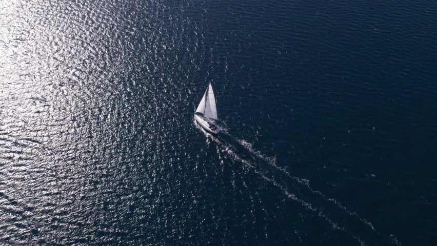 White sail boat cruising through blue sea with bright sunshine on surface, aerial Royalty-Free Stock Footage #1093901801