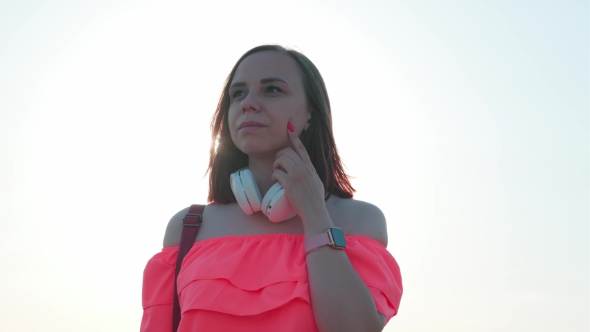 Young woman in bright dress with short hair in windy weather against sky on eve of sunset.