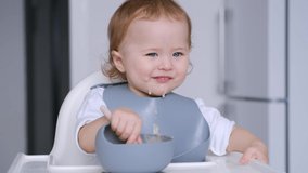 4K video Cute baby exploring food and learning self-feeding. Toddler sitting in a high chair at home, messy eating by himself, widely smiling showing teeth and appearing fangs.