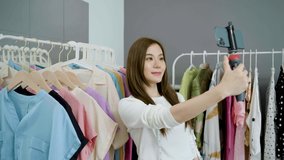 Young asian woman business owner at fashion store holding smartphone live streaming for sale fashion clothing. Blogger review clothes for presenting on social media. Online shopping