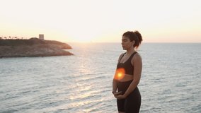 Young African American woman meditating in nature. Healthy yoga woman meditation at sunset. Young woman with curly hair relaxing at sunset wearing black sporsuit. Slowmotion video 4K 