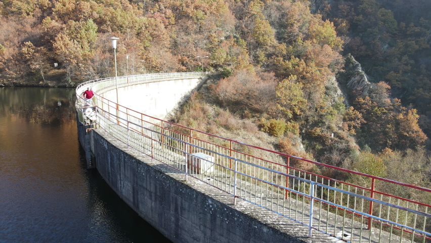 Aerial view of a dam bridge with the lake reflecting the colorful autumn forest in the background