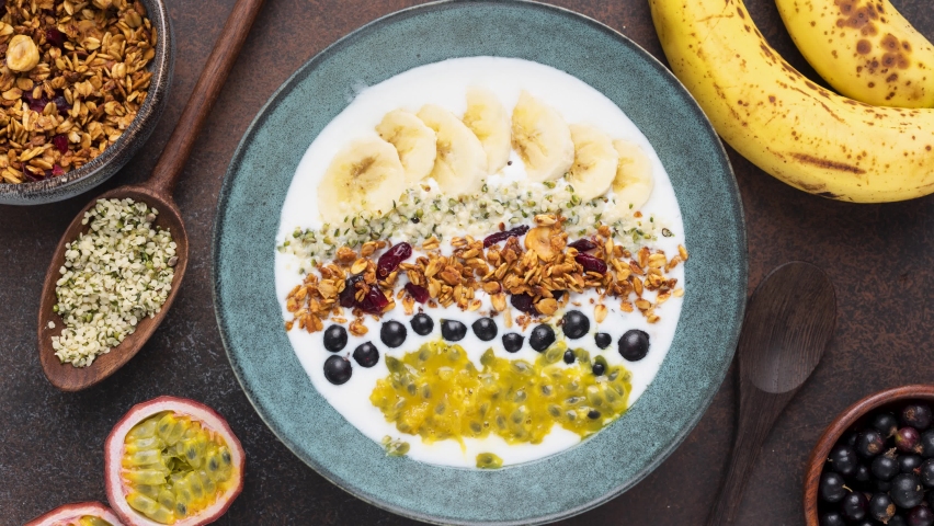 Stop motion animation. Yogurt Bowl with toppings Crunchy Oat Granola, Banana, Acai berry, Passion Fruit And Hemp Seeds. Top View | Shutterstock HD Video #1093909863