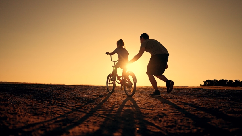 Happy family green park at sunset.Dad teaches daughter to rid bike in summer park.kid rides bicycle on green grass.Green energy.Dad teaches his daughter to ride bike for first time in park at sunset. Royalty-Free Stock Footage #1093911897