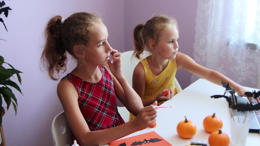selective focus on two schoolgirls, they watch a master class and a video lesson on a laptop, how to make Halloween decorations and sculpt a pumpkin from plasticine